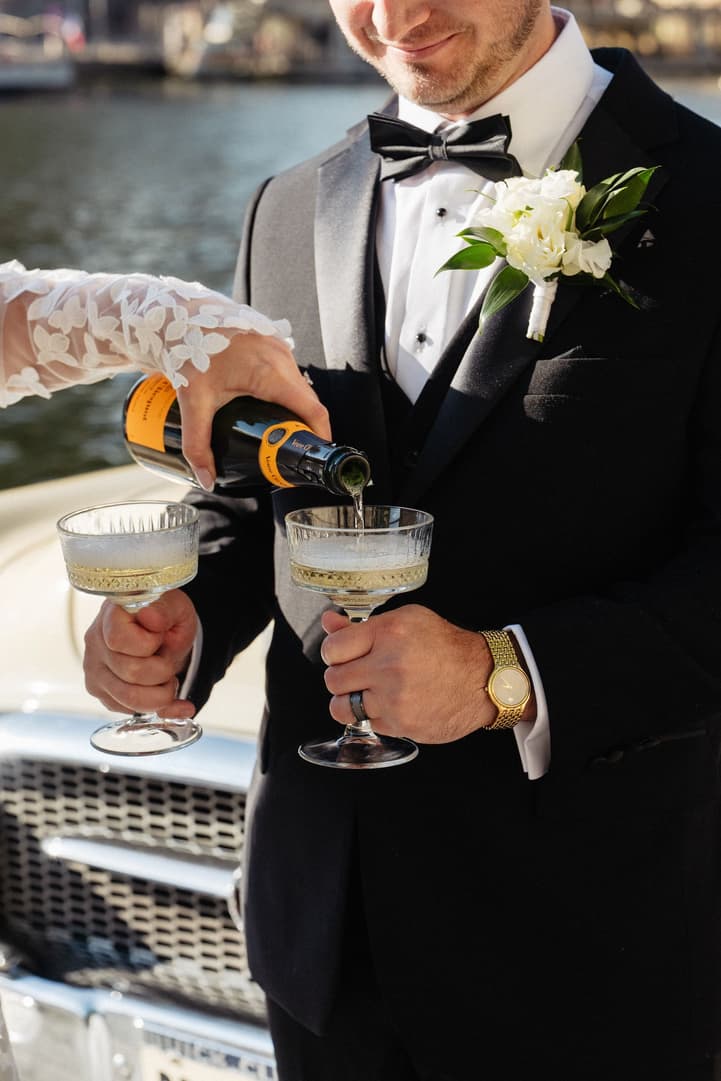 Victoria fills Tyler's coupe with Champagne beside the white vintage car by the Seine