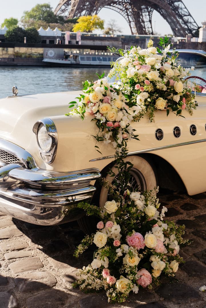 Flowers in white, ivory and pink cascade over the front of the white vintage car by the Seine