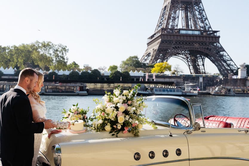 Victoria and Tyler cut their cake on the white vintage car by the Seine, the Eiffel Tower behind