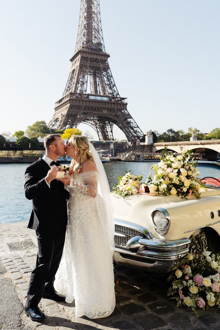 Victoria and Tyler kiss beside the flower-dressed white vintage car, the Eiffel Tower across the Seine