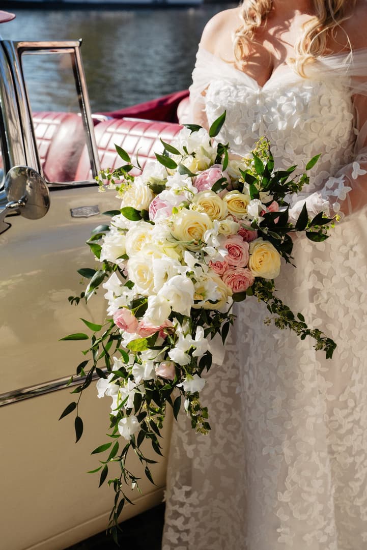 Victoria's cascading bouquet of white, ivory and pink flowers against her lace gown and the vintage car