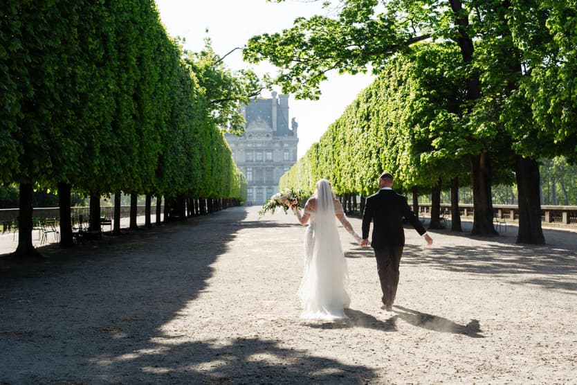 Victoria and Tyler walk together down the clipped allées of the Tuileries, the Louvre at the end
