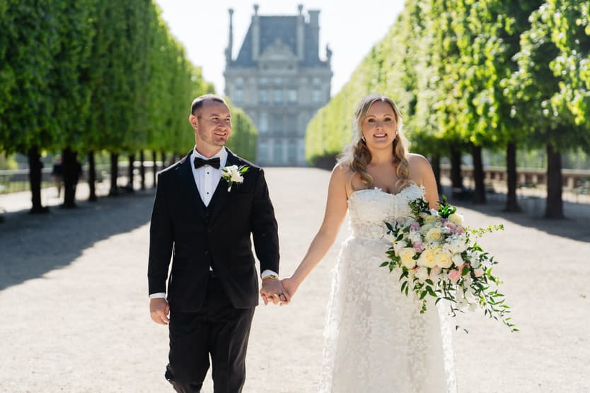 Victoria and Tyler walk hand in hand toward the camera through the Tuileries Garden