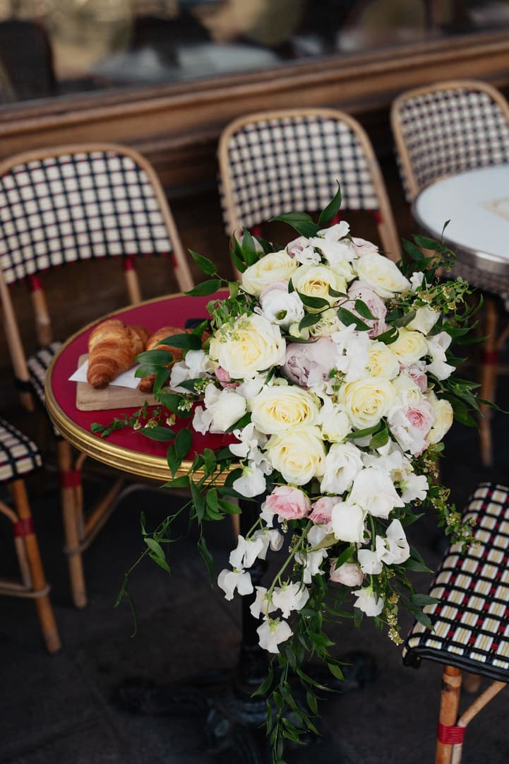 Victoria's cascading bouquet on a woven café chair at La Frégate, a croissant on the table
