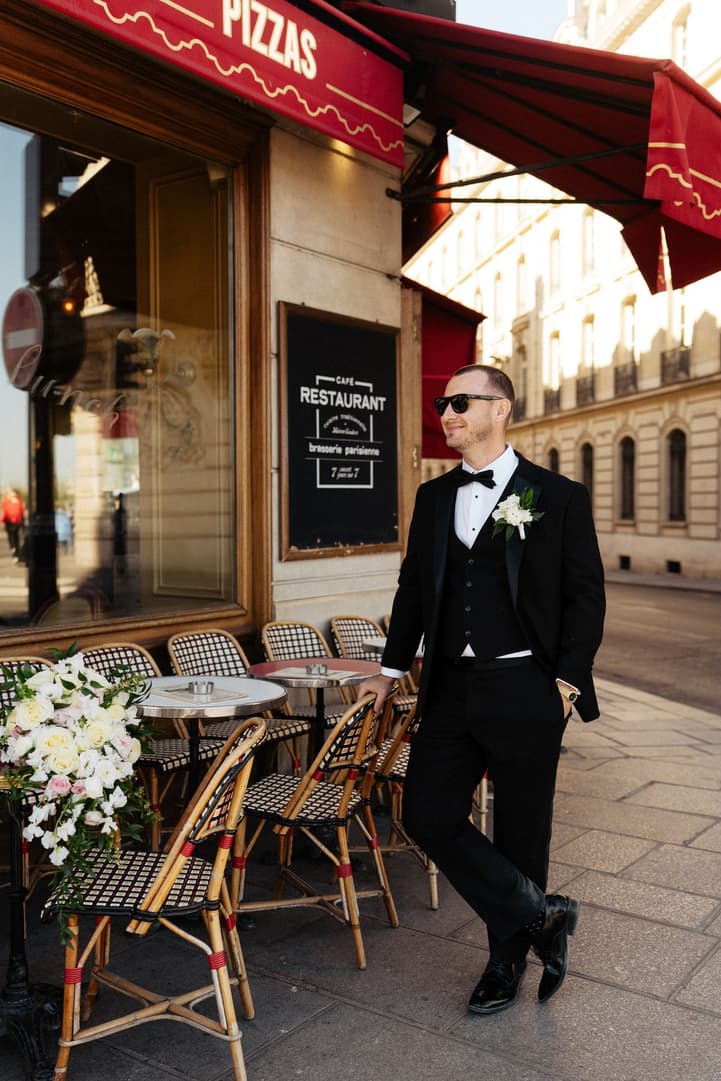 Tyler in sunglasses leans by the red awning of La Frégate, a café in Paris