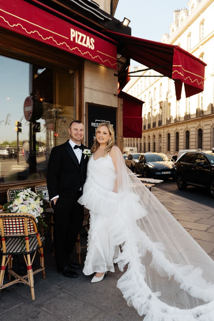 Victoria in her second look, a dramatic ruffle cape, beside Tyler at La Frégate's red awning