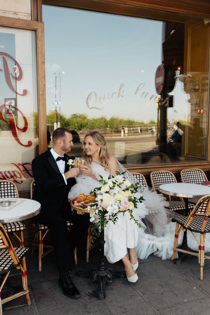 Victoria and Tyler toast with Champagne at a café table outside La Frégate in Paris