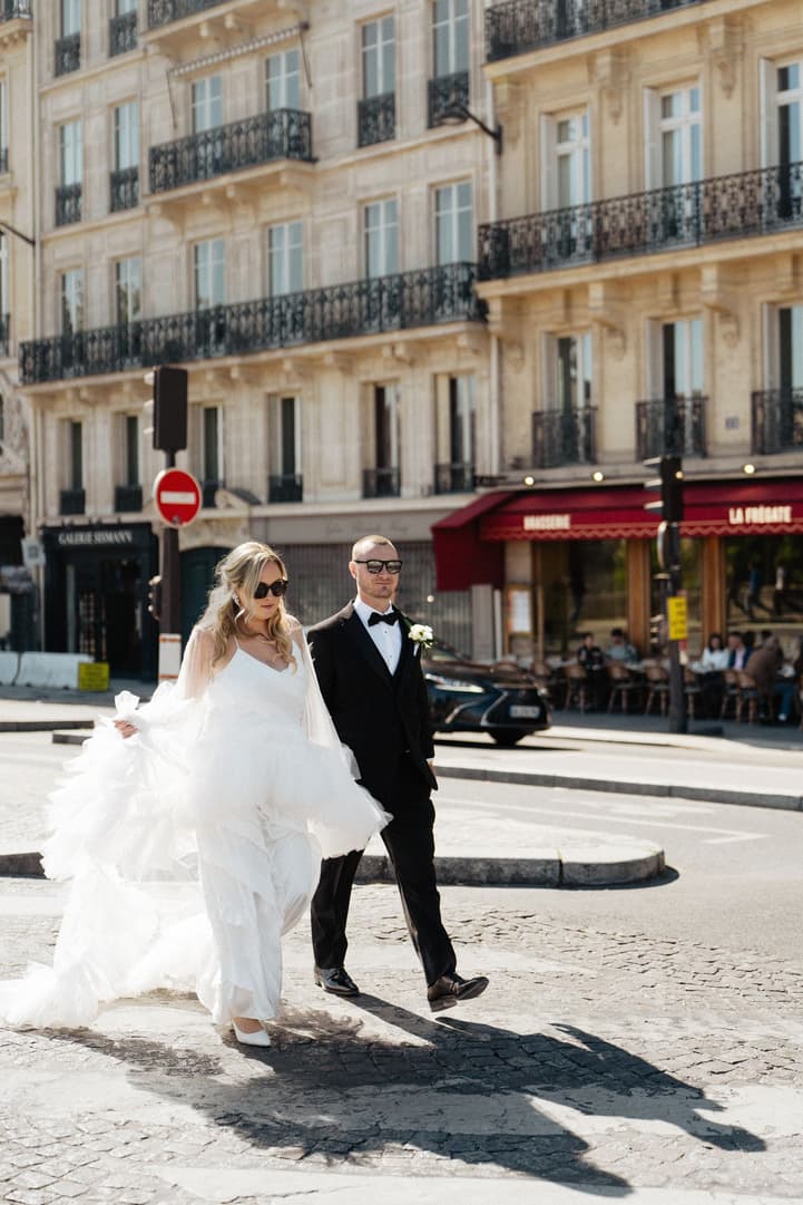 Victoria and Tyler in sunglasses cross a Paris street, La Frégate's red awnings behind them