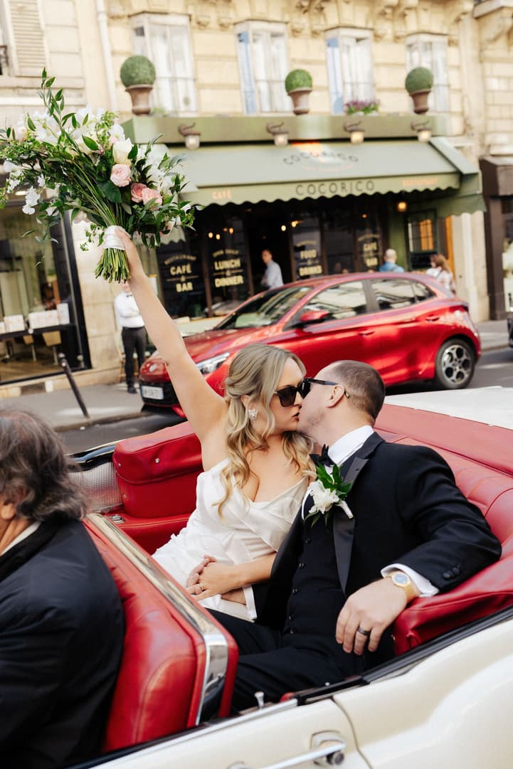 Victoria in her ruffle cape raises her bouquet and kisses Tyler in the red-seated white vintage convertible in Paris
