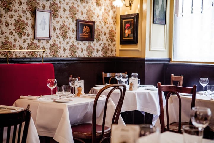 Allard's dining room: floral wallpaper, a red velvet banquette, dark wood panelling and white tablecloths