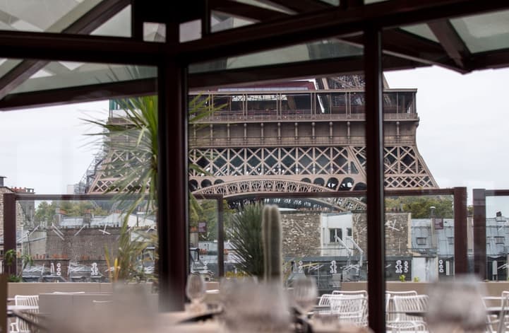 The Eiffel Tower through the glass walls of Les Ombres, laid tables in the foreground